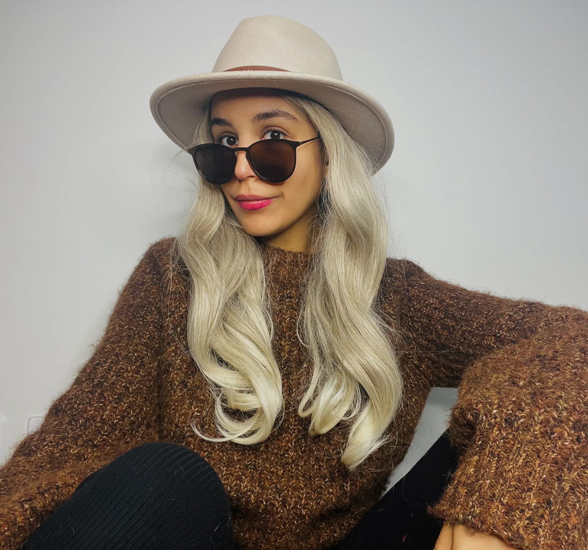 Dominique wearing a cream wide-brimmed hat, sunglasses and a brown knit sweater