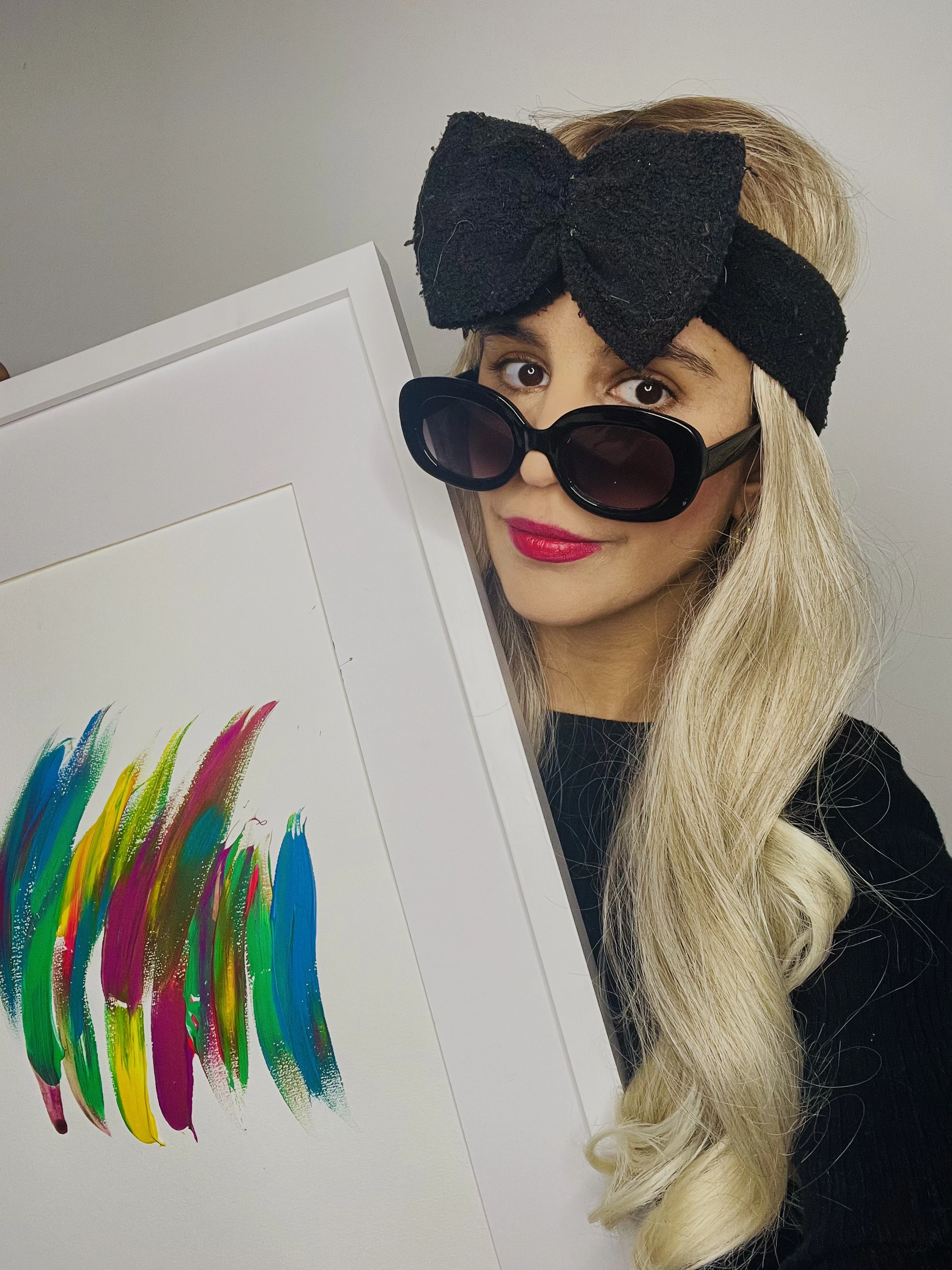 Portrait with a black bow and sunglasses, holding a colorful framed artwork